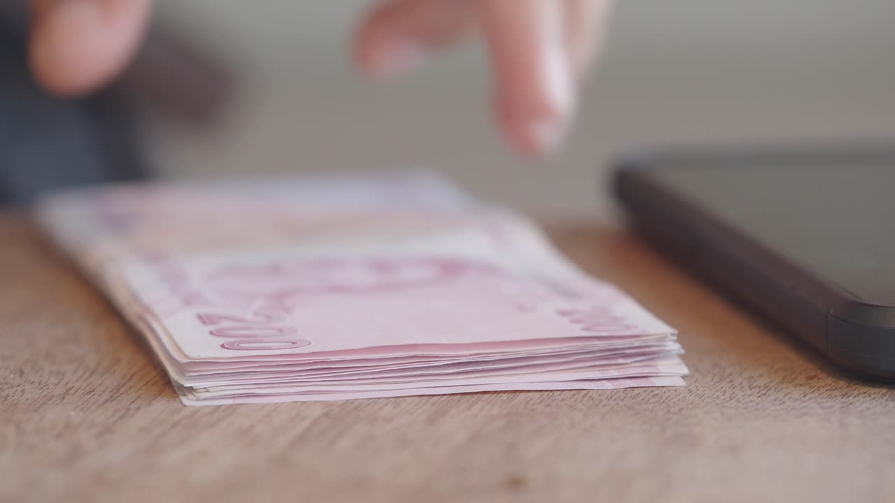 Person counting Turkish Lira banknotes on a wooden table