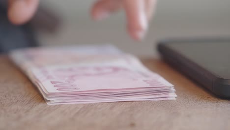person counting turkish lira banknotes on a wooden table