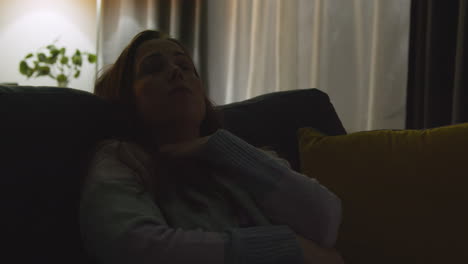 anxious or depressed woman sitting on sofa at home at night with lights turned off in the dark