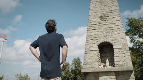 man walking to the stone cross on mountain and looking up to admire it