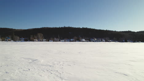 Fliegende-Drohne-über-Häusern-Und-Einem-Zugefrorenen-See-Im-Winter-In-Kanada