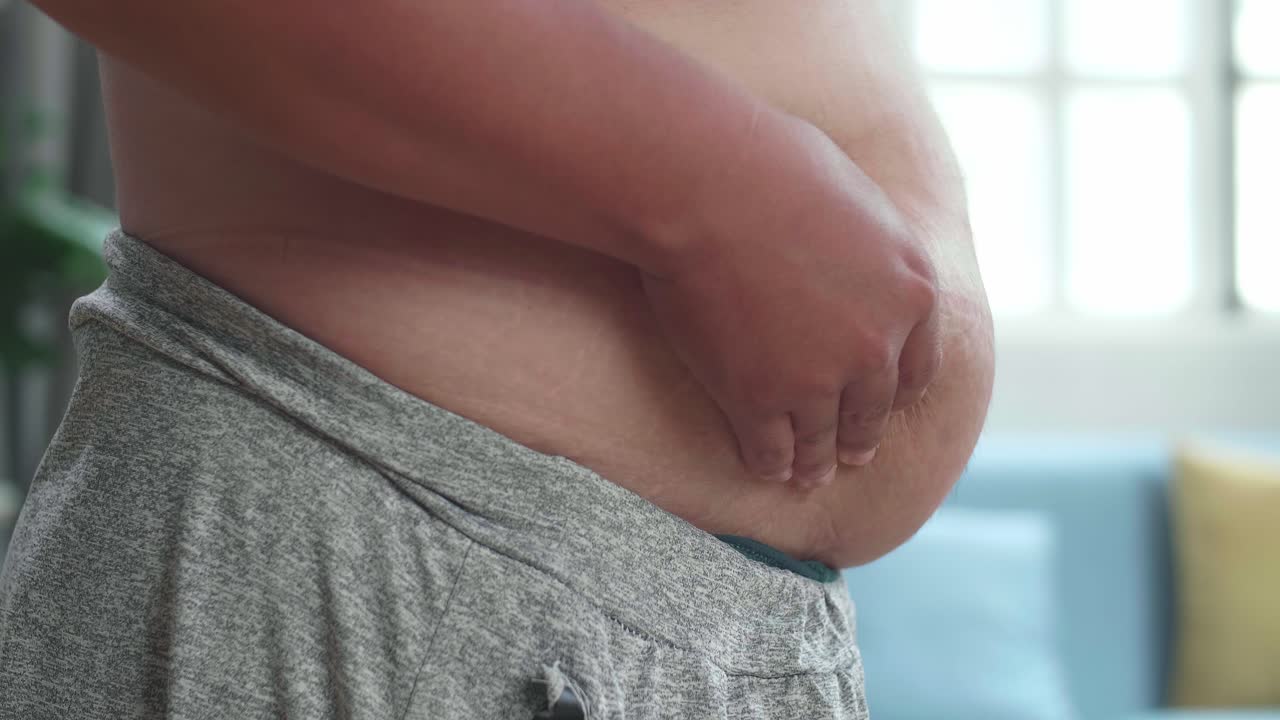 vista lateral de cerca del hombre gordo pellizcar el exceso de grasa que tiene alrededor de su cintura