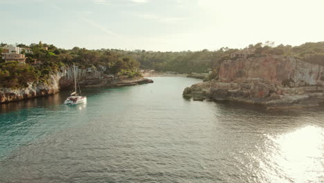 Barco-Catamarán-Flotando-En-Las-Tranquilas-Y-Brillantes-Aguas-Del-Mar-En-Cala-Llombards,-Mallorca,-España