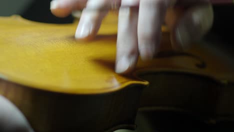 luthier meticulously varnishing a violin purfling and top plate with paintbrush and finger, skillfully antiquing to give a new instrument an aged, vintage and historic appearance while enhane beauty