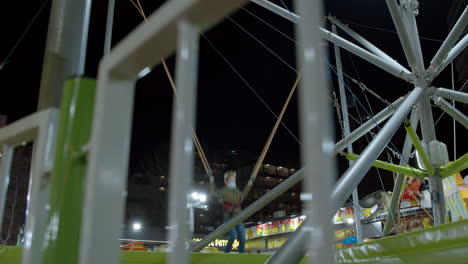 Boy-jumping-on-bungee-trampoline-in-funfair-at-night