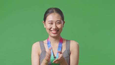 금메달을 달고 손을 박아주고 자랑스러워하는 아시아 여성이 스튜디오의 녹색 스크린 배경에서 첫 번째 우승자로 승리합니다.