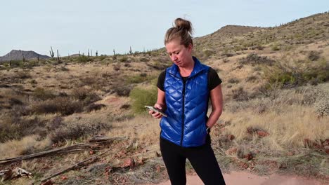 mujer revisando un teléfono inteligente en un paisaje desértico