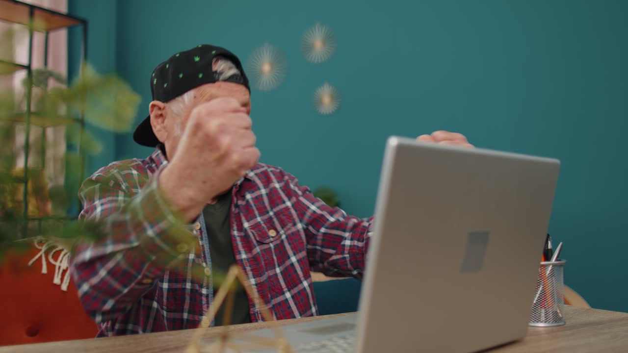 Grandfather man playing computer video games on laptop computer wins celebrate smiles happily