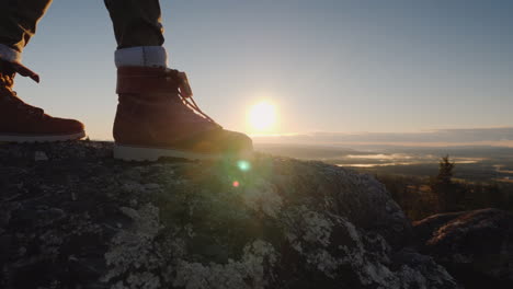 los pies del viajero en la cima del pico a través de ellos brilla el sol naciente y el hermoso paisaje