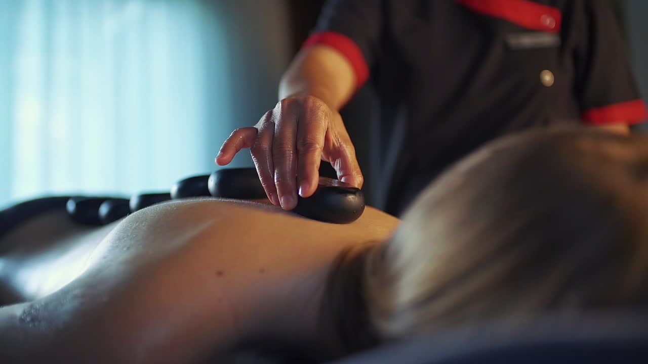 Massør lægger varm massagesten på pigens ryg. Slowmotion