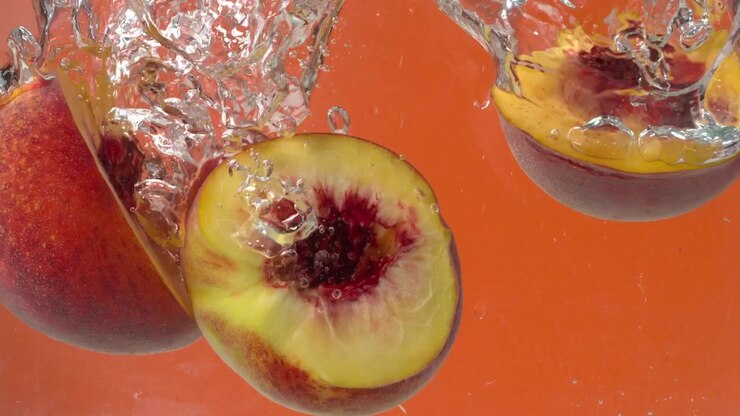 Pesche che cadono nell'acqua su sfondo arancione in macro al rallentatore