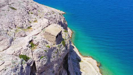 Aerial-view-of-sheep-on-Pag-Island-entering-small-stone-shelter-on-rocky-bluff