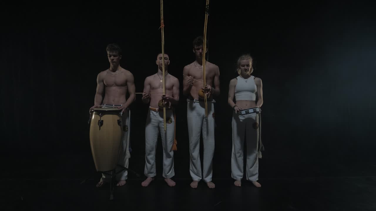 группа профессиональных танцоров практикует капоэйру в темноте под прожектором на черном фоне студии. афро-бразильское боевое искусство, которое сочетает в себе элементы танца.