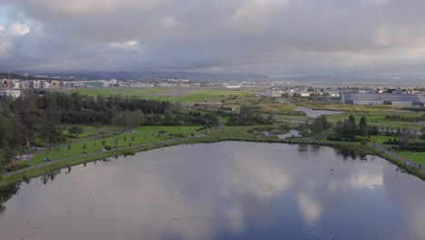 Lago-Tjörnin-Con-Reflejo-De-Nubes-En-La-Superficie,-Distante-Aeropuerto-De-Reykjavik