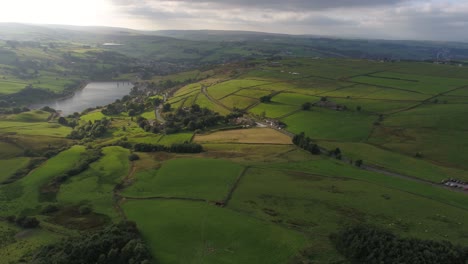 Beautiful-late-evening-drone-footage-with-a-mixture-of-sun-and-cloud-showing-the-rural-West-Yorkshire-hills-and-countryside-including-farms,-reservoir,-stone-walls,-country-roads-and-moving-vehicles