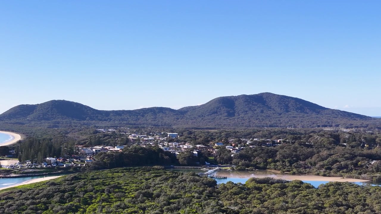 Laaja ilmakuva rannikkokaupungista, rehevästä metsästä ja vuorista South West Rocksissa, Australiassa
