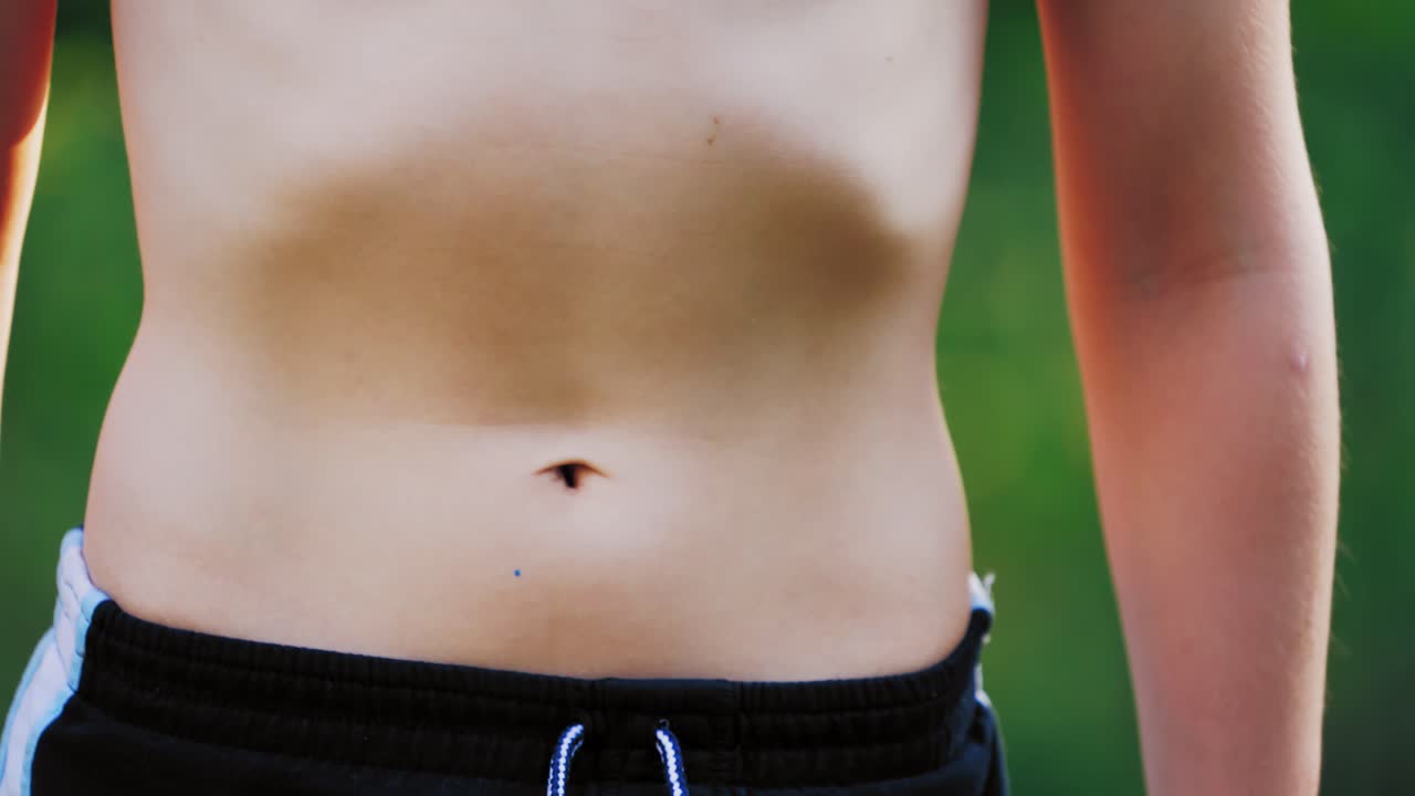 Bare stomach of a young boy outdoors. Healthy boy in sport pants does exercises breathing by his belly. Close-up.