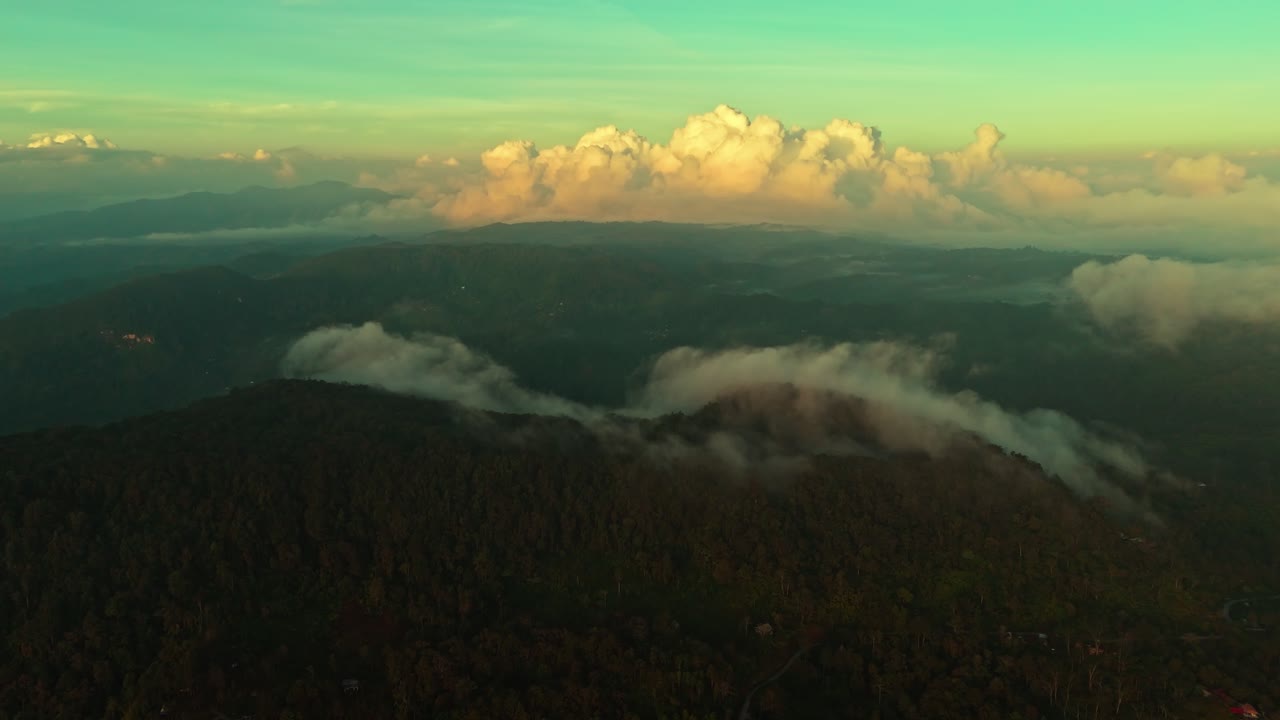 Cinematic drone shot of forested mountains with drifting mist and golden clouds on the horizon at sunset. Ideal for travel, nature, and cinematic storytelling