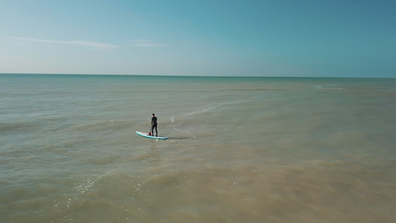 drone círculos joven stand up paddle surf en el mar con acantilados blancos de dover en el fondo