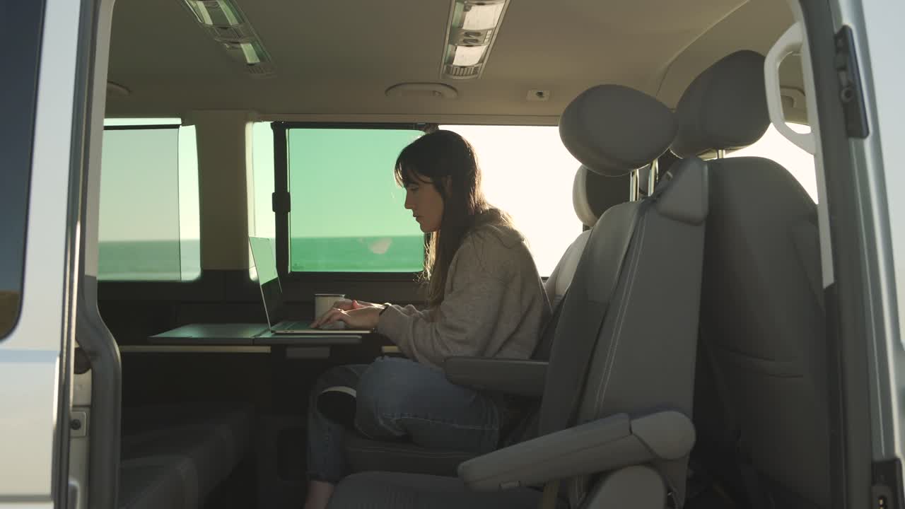 Donna in viaggio che lavora al laptop in un furgone