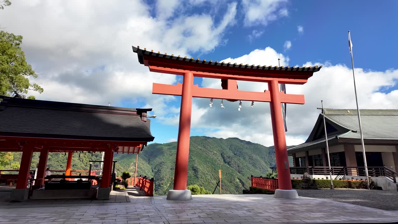 Scenic view of the iconic red torii gate at the entrance of Kumano Nachi Taisha, a significant Shinto shrine nestled in the mountains of Nachikatsuura, Japan. Pan Left
