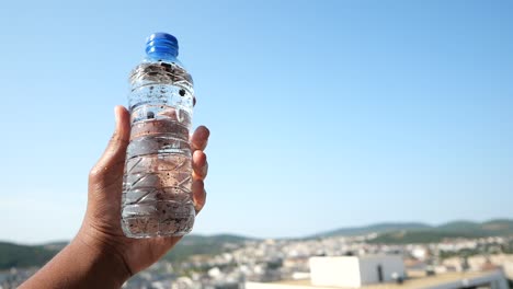 persona sosteniendo una botella de agua con una ciudad en el fondo