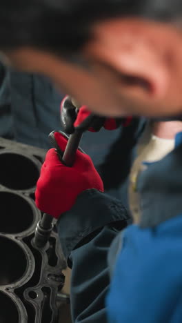 primer plano de la nuez de aflojamiento mecánica con guantes rojos mientras otro observador con guantes blancos se encuentra cerca en el taller, centrándose en el trabajo detallado del motor del automóvil