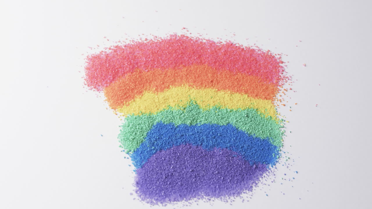 Video of close up of rainbow coloured sand grains and copy space on white background