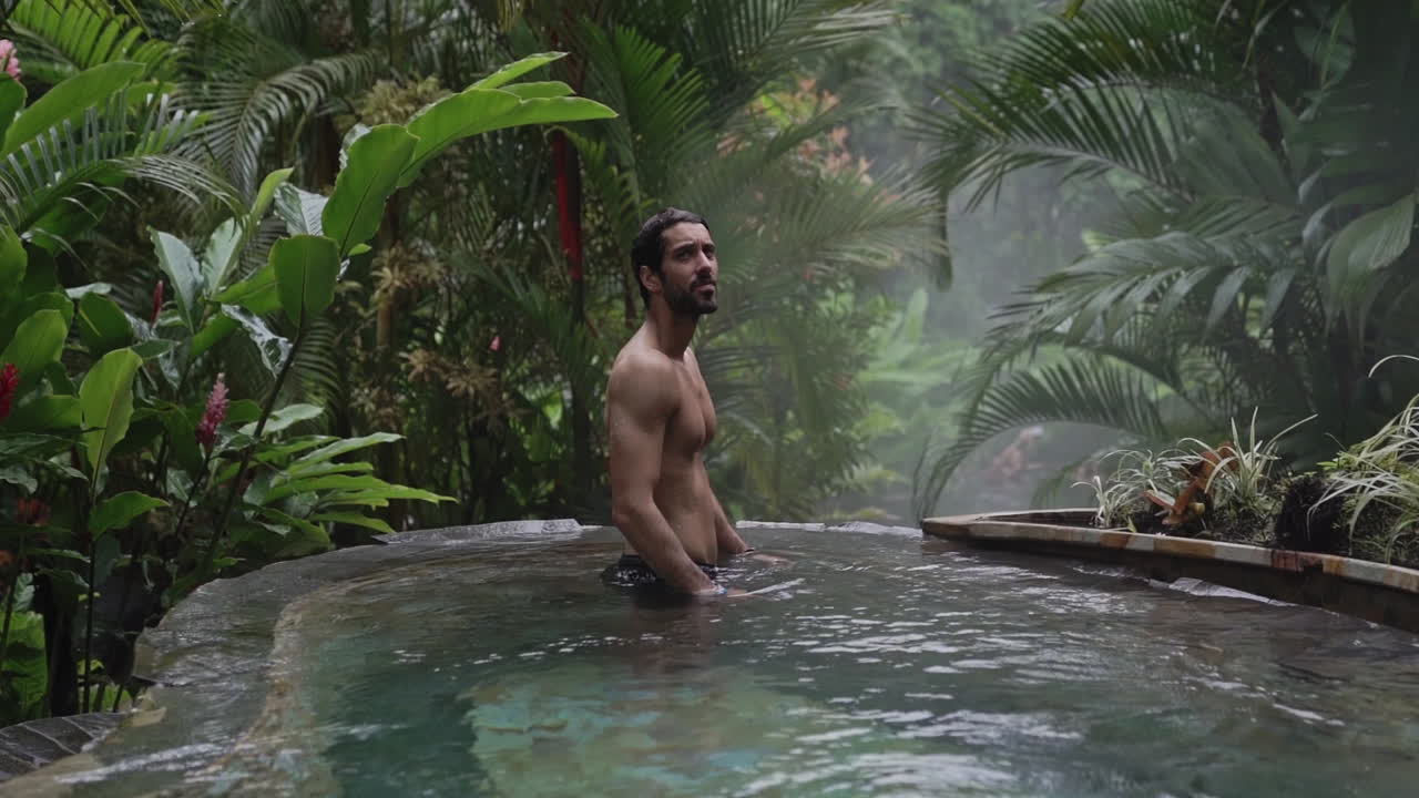 난간 위로 떠오르는 샷은 열대 우림의 고급 수영장에 있는 남자를 보여줍니다, 슬로우 모션