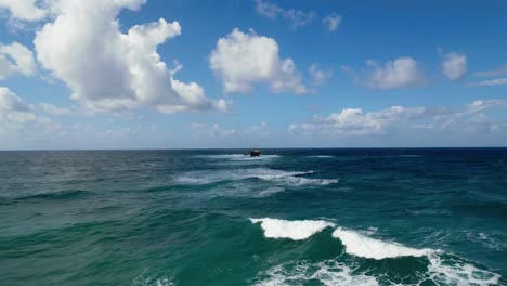 Mar-Azul-Ondulado-Con-Naufragio-En-El-Centro-Bajo-Un-Cielo-Parcialmente-Nublado,-Frente-A-La-Costa-De-Chipre