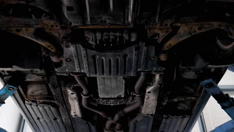 the underneath of a rusty used car up in a workshop lift. pan down shot in 4k.