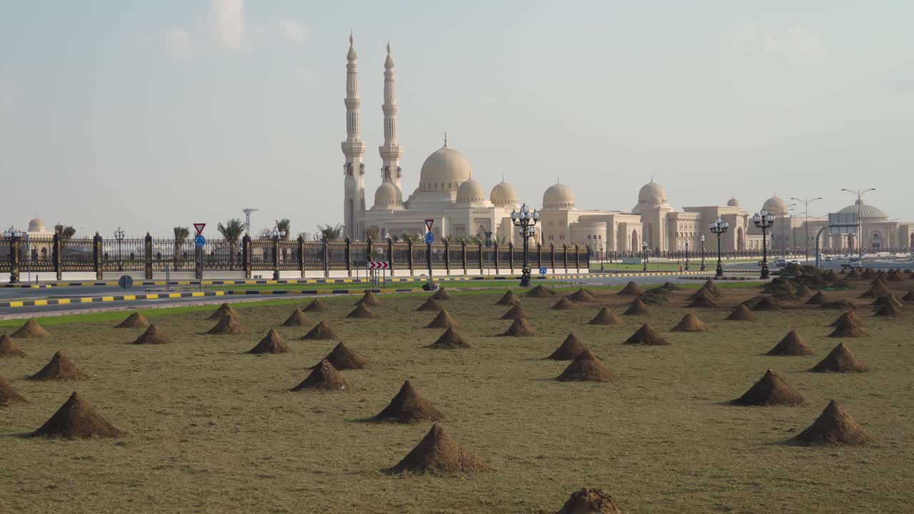 pequeños montones de arena en el campo con la universidad al qasimia y la mezquita al fondo - ciudad de sharjah, emiratos árabes unidos - lateralmente