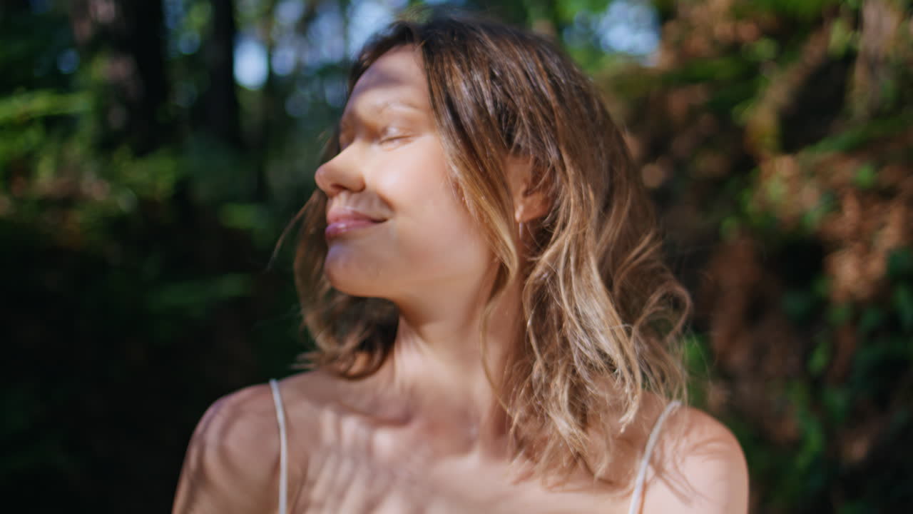 Smiling woman warming sunlight in park looking camera. Girl touching hairstyle