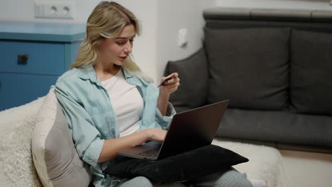 Mujer-Rubia-Sentada-En-Casa-Comprando-En-Una-Tienda-De-Internet-Usando-Una-Computadora-Portátil-Con-Tarjeta-De-Crédito