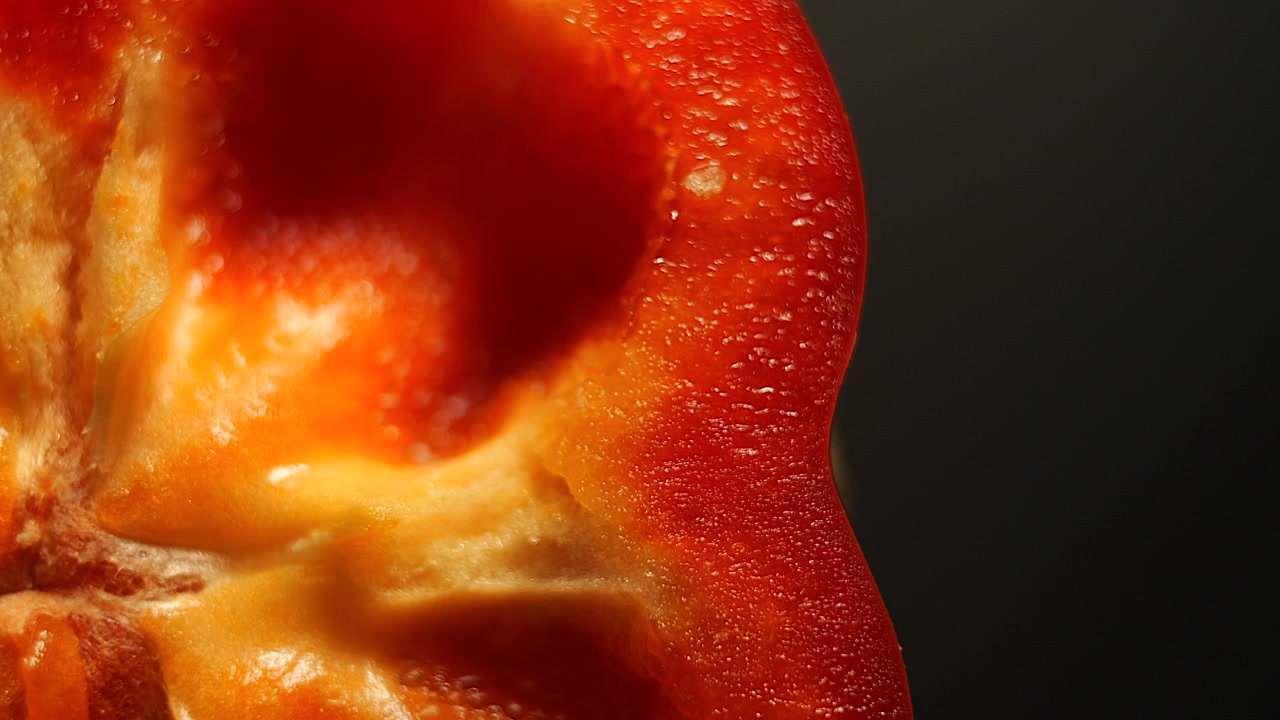 Scatto dall'alto con obiettivo macro 50p di una fetta di peperone rosso che ruota per rivelare la texture e il colore naturale vibrante