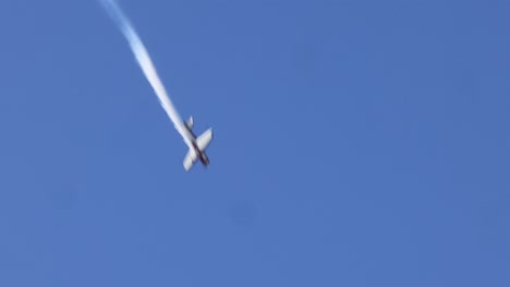 plane executes maneuvers with smoke trails in blue sky