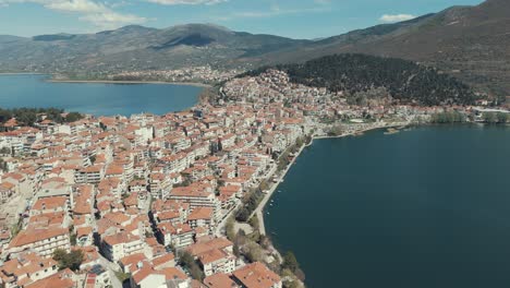 drone flying above a village on a green hill in europe, red roof tops, little houses, sunny weather, blue water lake, greece 4k video