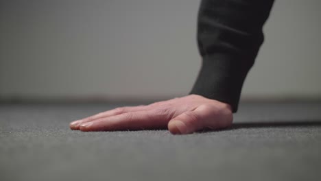 male caucasian hand touching a gray floor surface with a neutral gray background