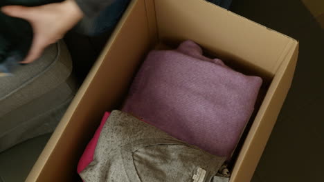 woman packing folded clothes into cardboard box selling clothing online store sale