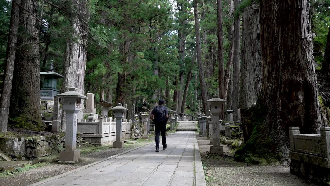 mochilero masculino solitario caminando por el camino a través del cementerio del bosque zen en japón