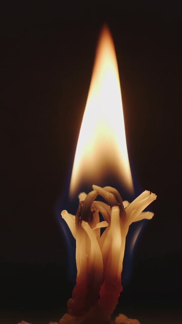 Vertical video: Burning braided wick and flame elongating charring wax feeding flame in close-up