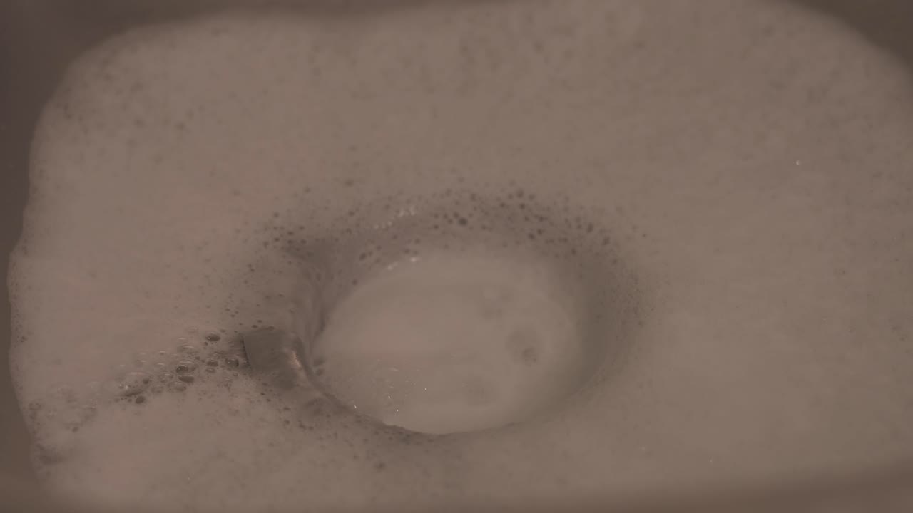 Close-up shot of soapy water running down the sink as a person washes dishes, capturing a common household cleaning task.