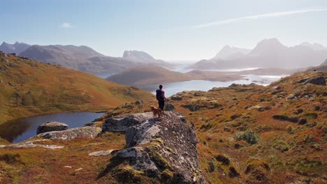 Luftumlaufbahn-Um-Eine-Schöne-Junge-Wanderin-Und-Ihren-Golden-Retriever-Hund,-Die-Die-Aussicht-Auf-Der-Wanderung-Zum-Kvalvika-Strand-Bewundern,-Blauer-Vogeltag,-Lofoten-Inseln,-Norwegen