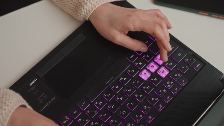 Closeup hands typing rgb laptop keyboard, cozy sweater sleeves, colorful backlight shifting across keys, rapid finger movement, remote developer and content creator workflow, ambient desk