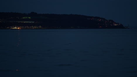 ferry drives along edge of waterway below coastal town and mountain