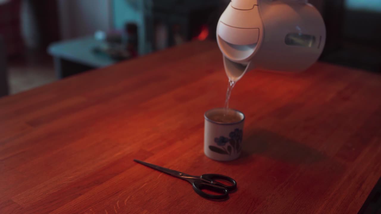 verter agua caliente en una taza de té sobre la mesa en casa con unas tijeras a un lado