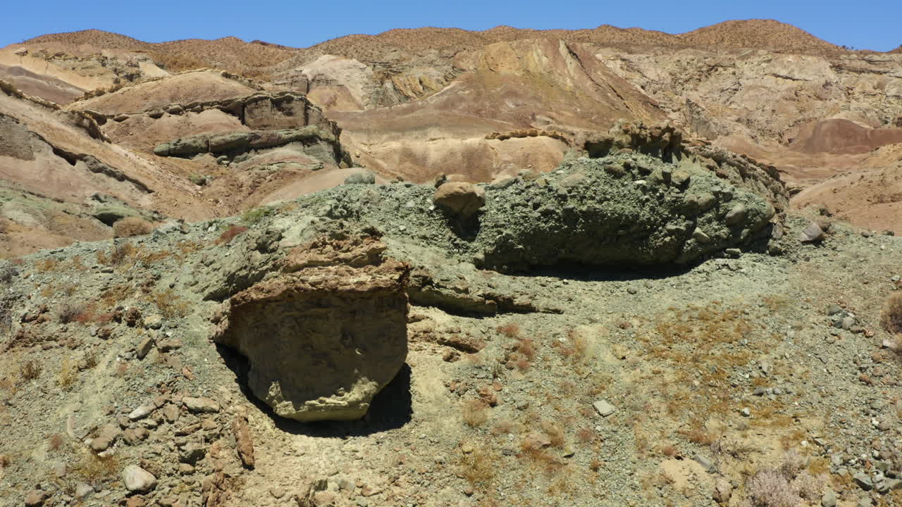 volando sobre las montañas rocosas para revelar un camino de tierra que serpentea a través del paisaje en la distancia y capas de formaciones geológicas