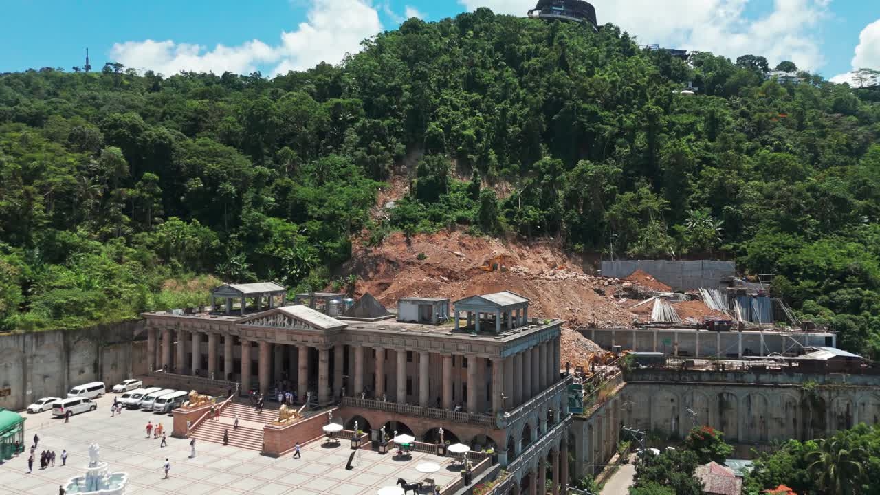 Stunning aerial view of a historic colonial-style building under renovation surrounded by lush green hills, tropical houses,and blue sky, ideal for travel, tourism,architecture, and cultural heritage