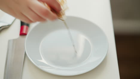 chef hands setting peeled sausage casing onto white plastic plate on bright kitchen table, highlighting delicate handling of translucent meat casing and clean minimal culinary workspace