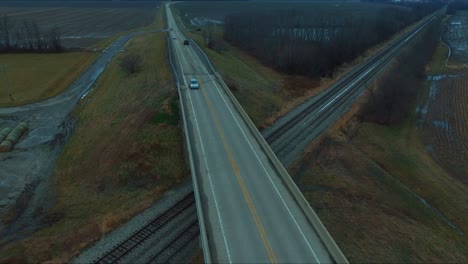 Cars,-trucks-and-a-bus-traveling-across-an-overpass-running-over-railroad-tracks-next-to-a-pond-on-a-rural-Illinois-highway